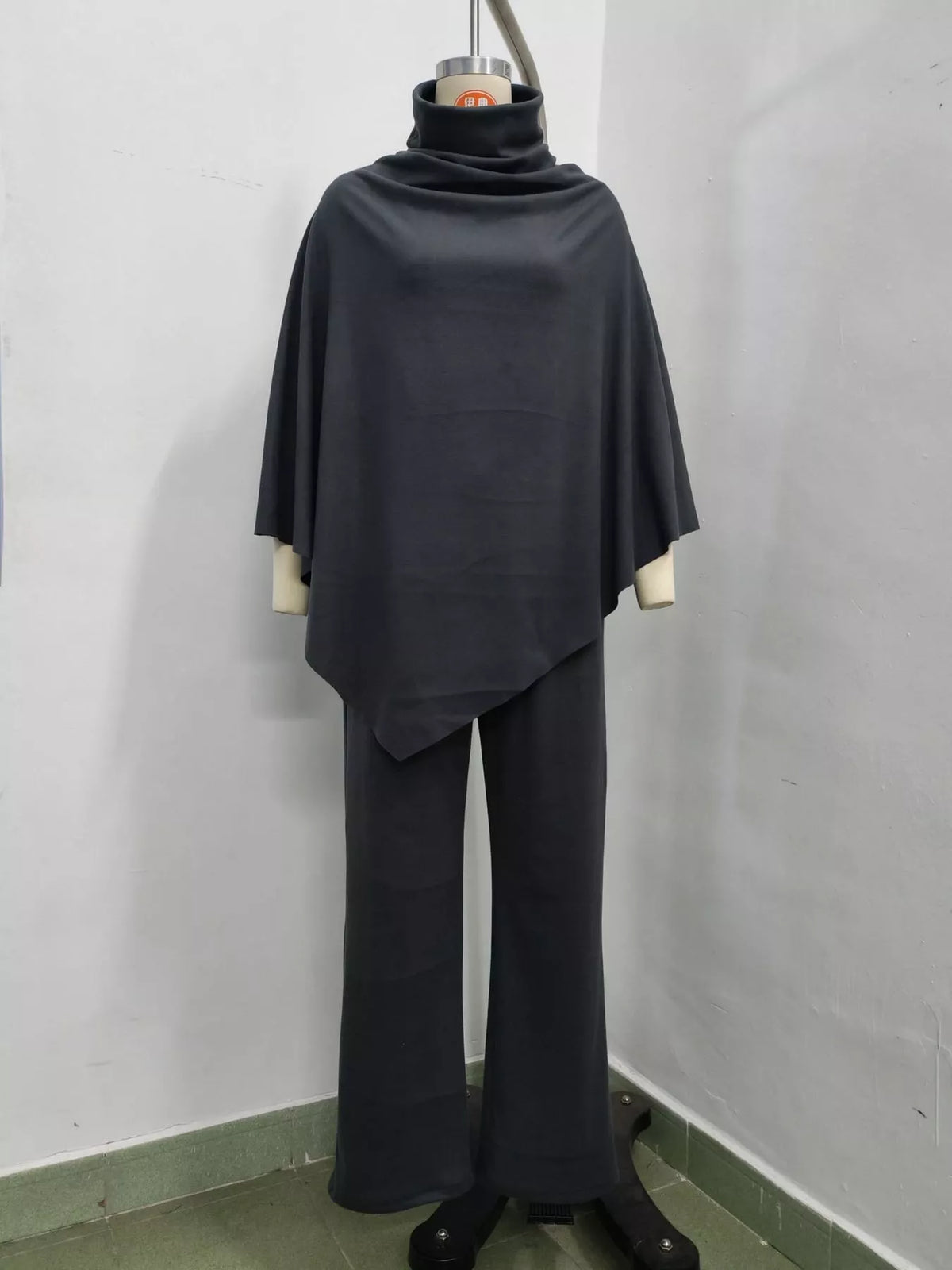 A dark charcoal gray two-piece set consisting of a draped turtleneck poncho top and matching wide-leg pants, displayed on a dress form mannequin against a plain white wall.