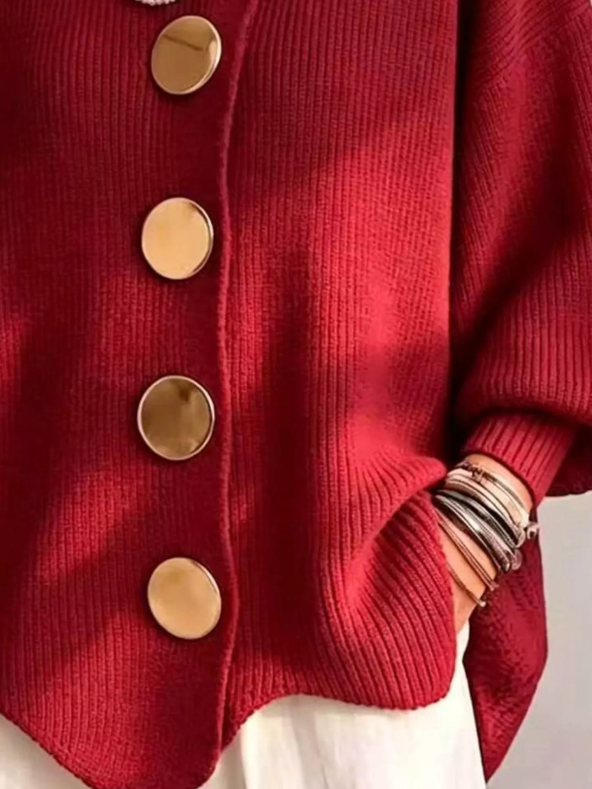A close-up of a red ribbed knit cardigan sweater with large round gold buttons, worn over a white garment. The person&