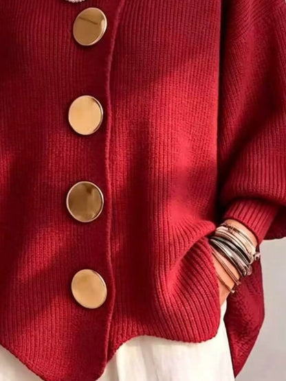 A close-up of a red ribbed knit cardigan sweater with large round gold buttons, worn over a white garment. The person&