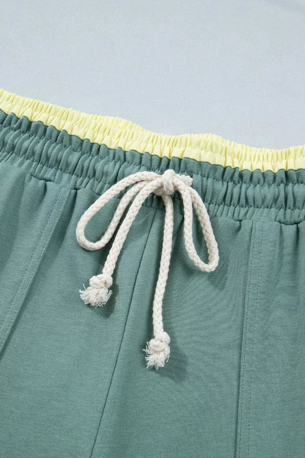 Teal shorts with a yellow waistband and white drawstring on a light blue background