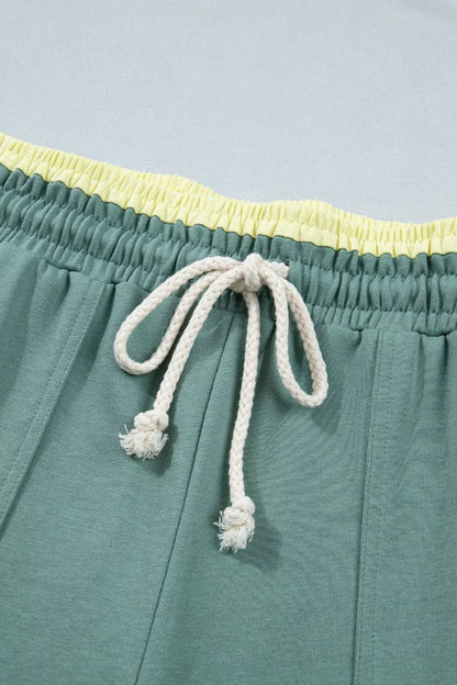 Teal shorts with a yellow waistband and white drawstring on a light blue background