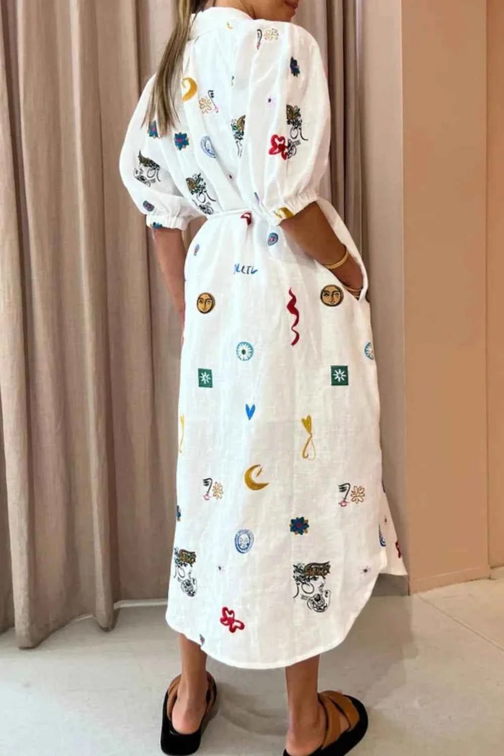 Person wearing a white dress with colorful patterns against a beige curtain background
