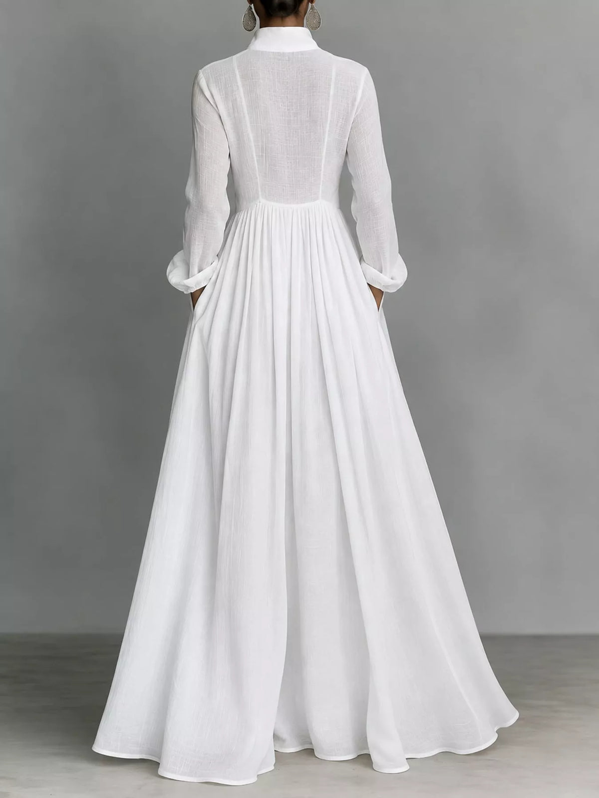 A model posing in a white long-sleeve button-front maxi dress featuring a V-neckline, Victorian-inspired sleeves, and a relaxed, flowy silhouette.