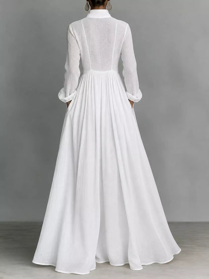 A model posing in a white long-sleeve button-front maxi dress featuring a V-neckline, Victorian-inspired sleeves, and a relaxed, flowy silhouette.