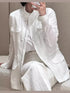 Woman wearing a white long-sleeve linen utility jacket with front flap pockets and matching white pants against a neutral studio background.