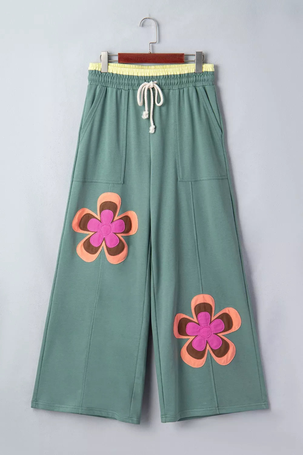 Green pants with pink flower designs on a hanger against a light gray background