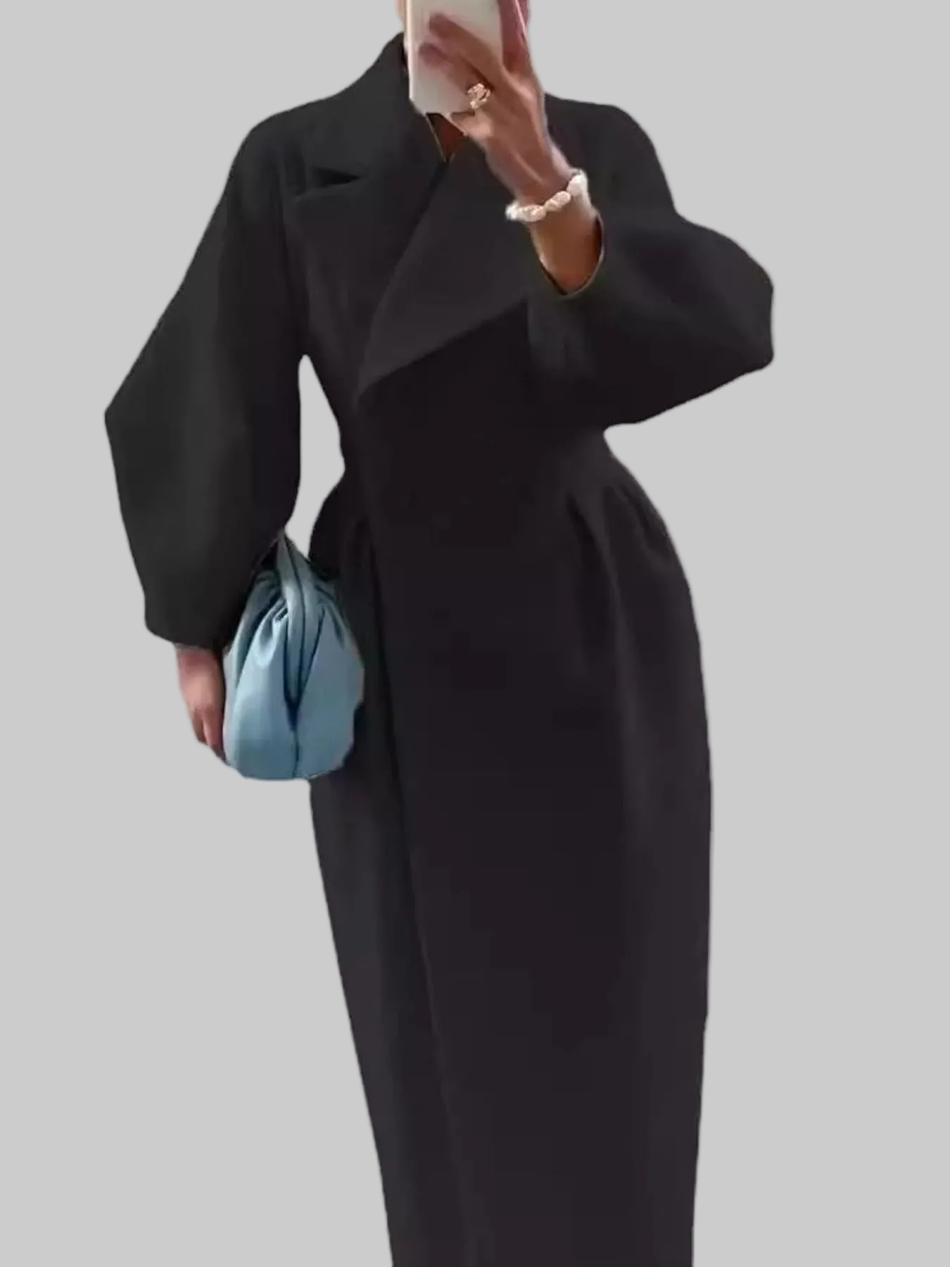 Person wearing a long black coat holding a blue handbag on a white background