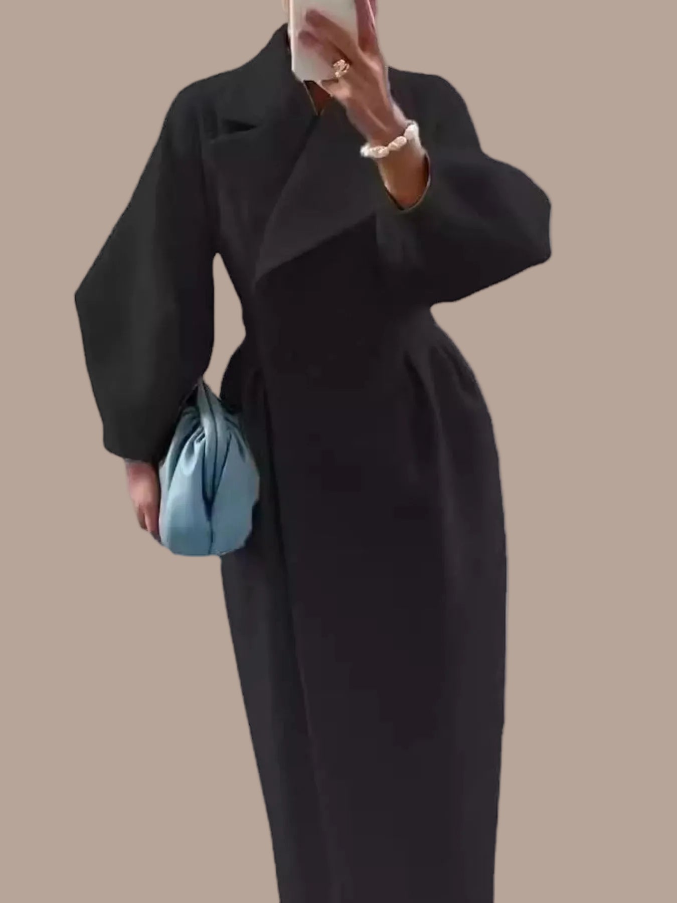 Person wearing a long black coat holding a blue handbag on a white background