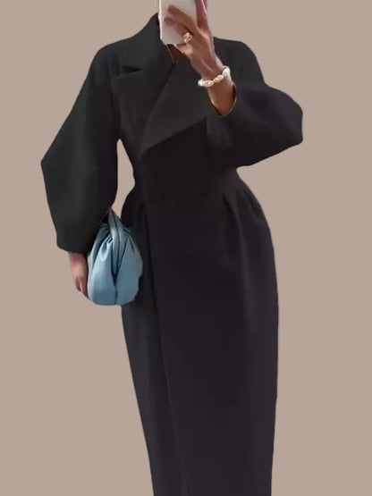 Person wearing a long black coat holding a blue handbag on a white background