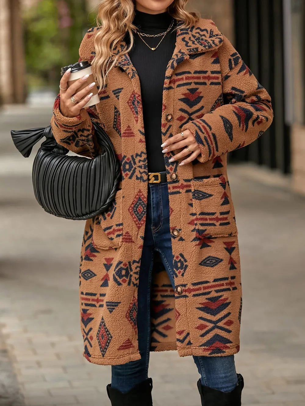 Person wearing a patterned coat holding a black handbag on a street.