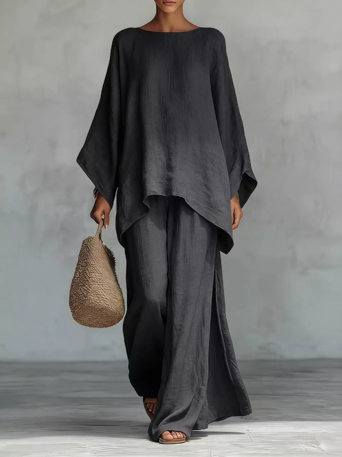 Person wearing a dark gray outfit holding a woven bag against a plain background