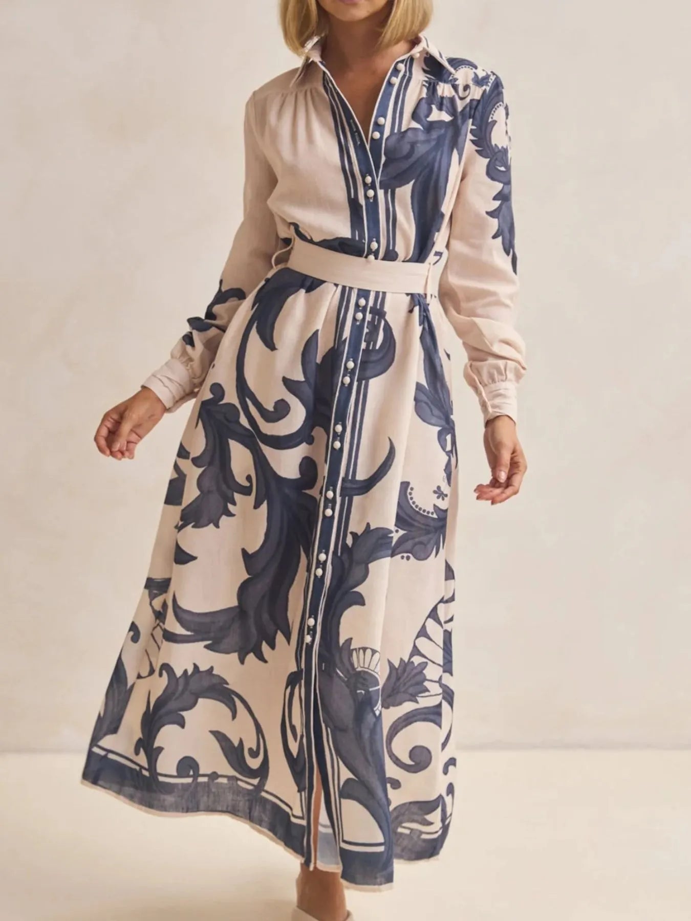 Woman wearing a long dress with blue floral pattern on a plain background