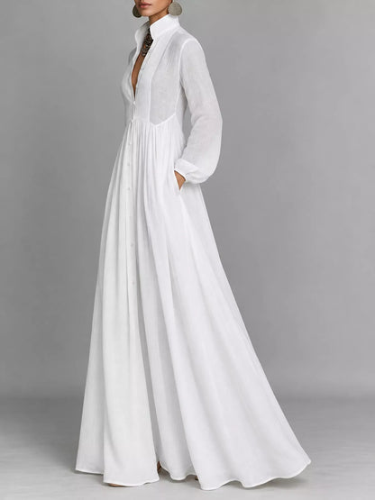 A model posing in a white long-sleeve button-front maxi dress featuring a V-neckline, Victorian-inspired sleeves, and a relaxed, flowy silhouette.
