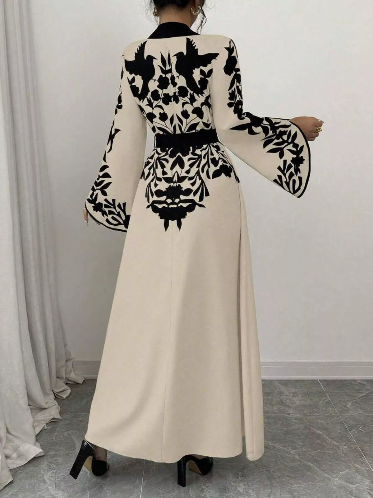 Beige dress with black floral patterns worn by a person, standing against a white wall.