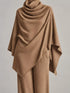A camel brown draped knit poncho or shawl styled over matching wide-leg trousers, shown on a mannequin against a neutral light gray background.