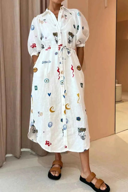 Person wearing a white dress with colorful patterns in a room.