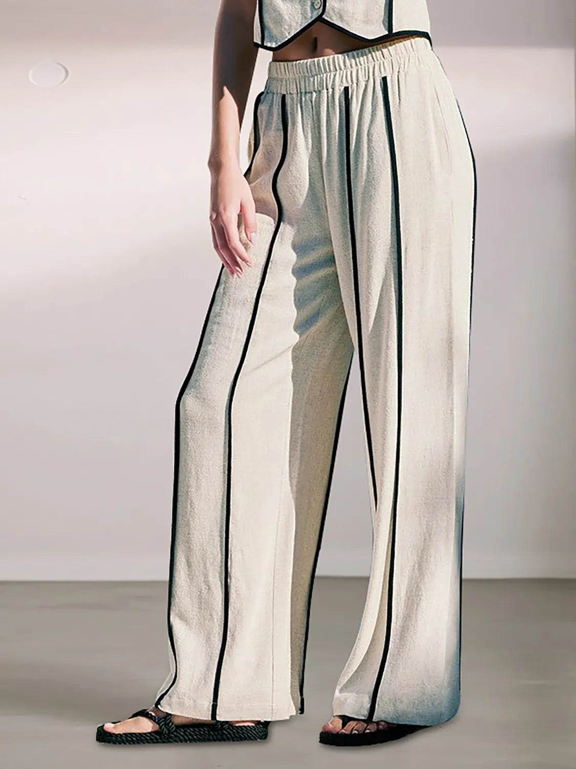 Person wearing a stylish outfit with wide-leg pants and a top on a plain background