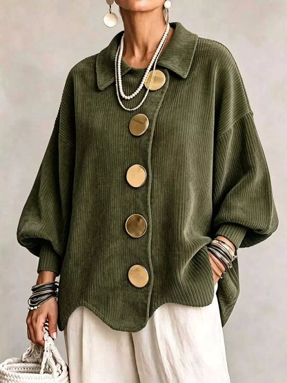 An olive green corduroy button-up cardigan with oversized round gold-tone buttons, worn by a model with white pants, layered pearl necklaces, and bracelets.