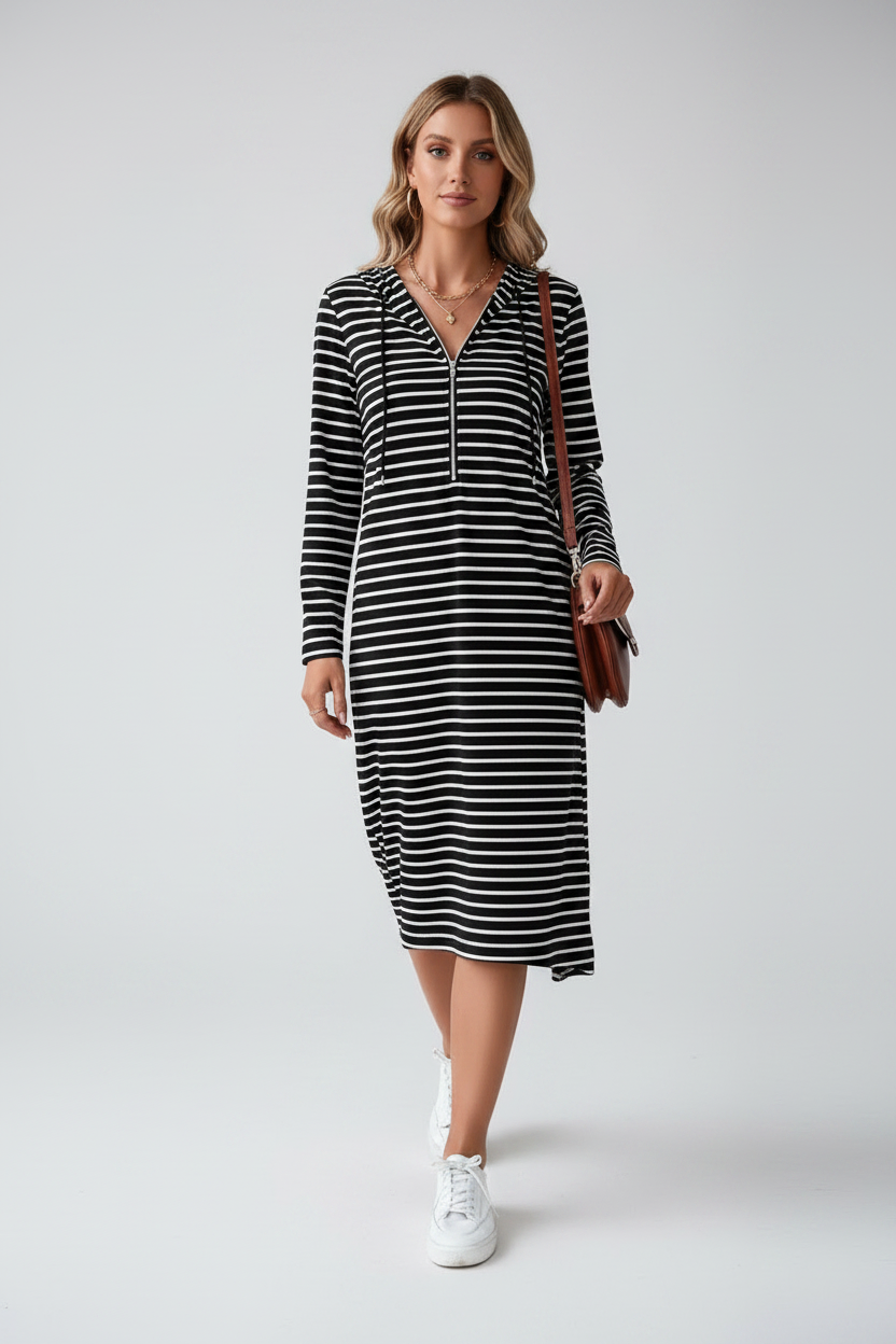 A woman modeling a black and white horizontally striped long-sleeve midi dress with a half-zip neckline, paired with white sneakers and a brown shoulder bag, against a light gray studio background.