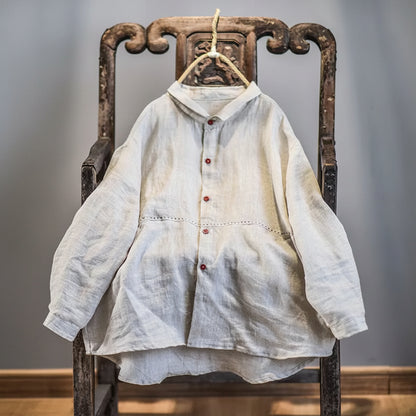 A light beige linen long-sleeve button-up shirt with red buttons, hanging on a rustic wooden chair.