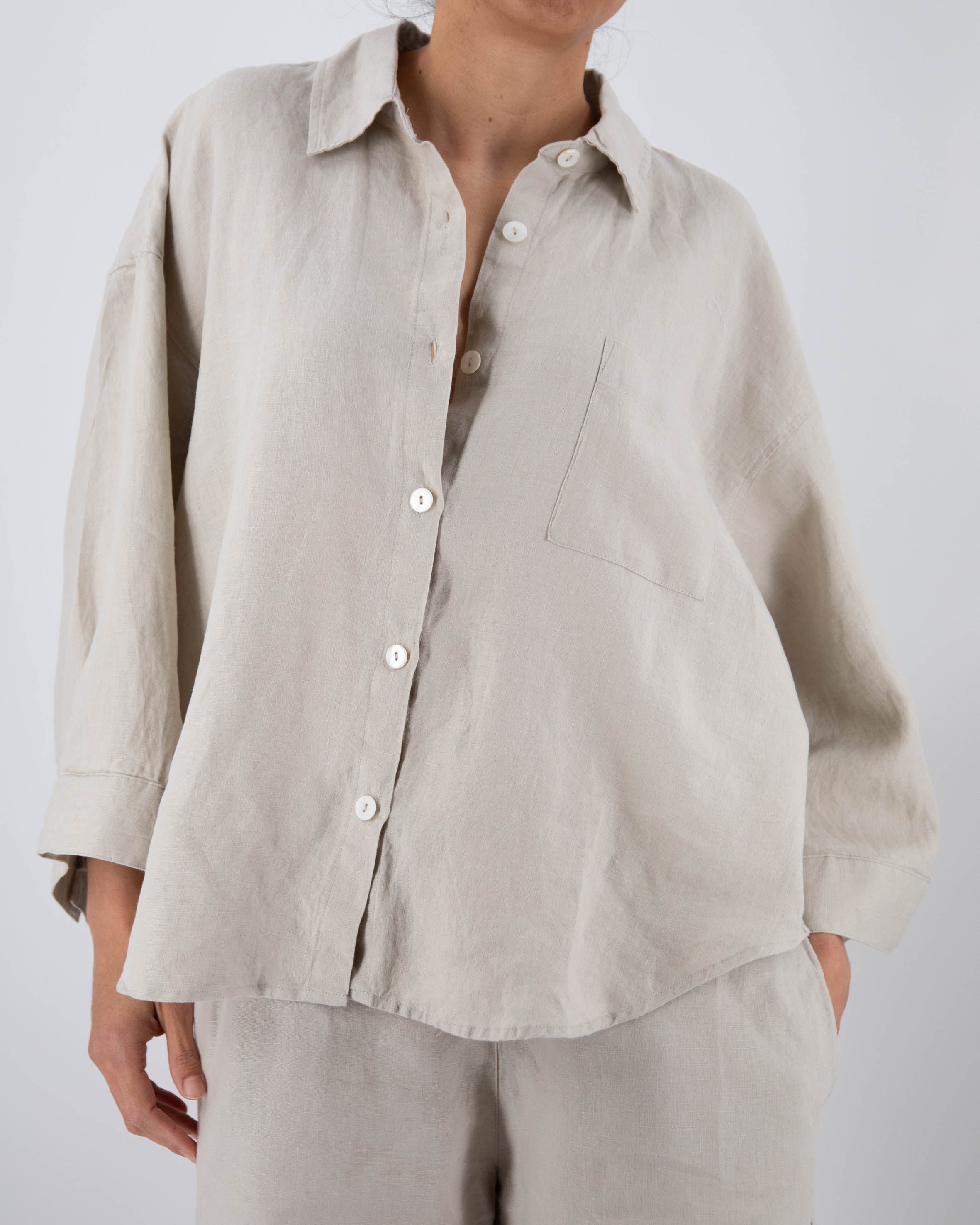 Person wearing a beige button-up shirt and pants on a white background