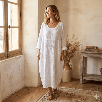 Woman in a white dress standing in a room with wooden floor and window.