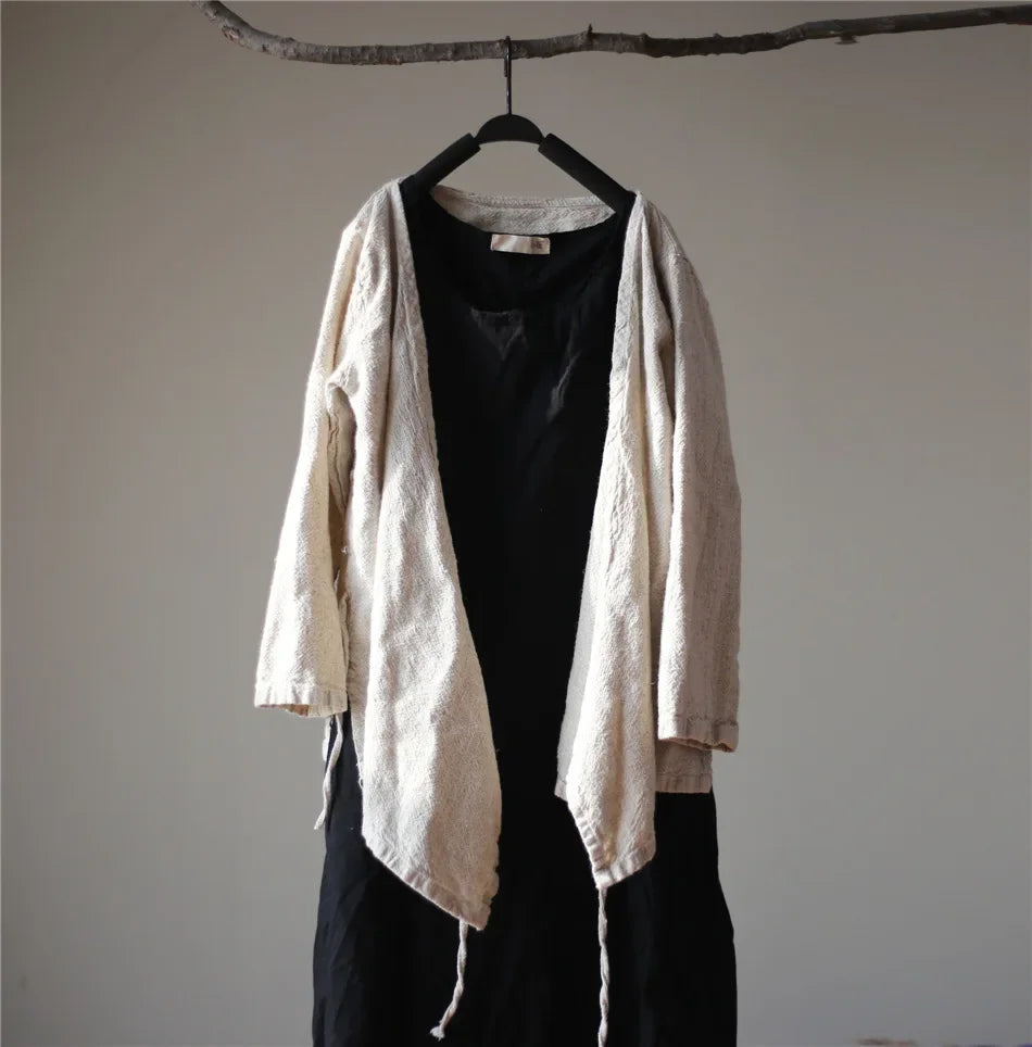 Beige cardigan over black top and pants on a hanger against a plain wall.