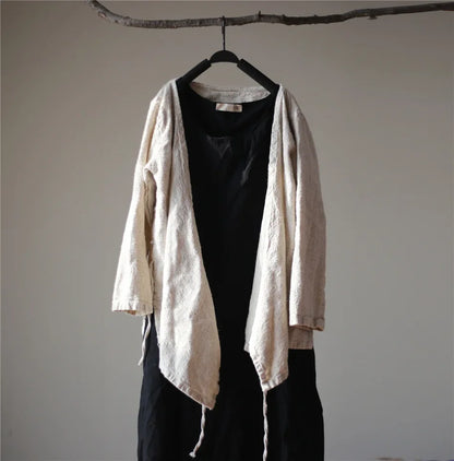 Beige cardigan over black top and pants on a hanger against a plain wall.