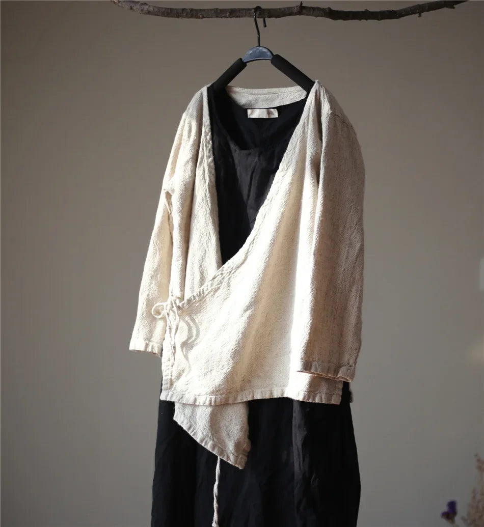 Light-colored jacket over a black shirt and pants on a hanger against a plain wall.