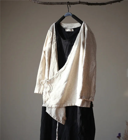 Light-colored jacket over a black shirt and pants on a hanger against a plain wall.