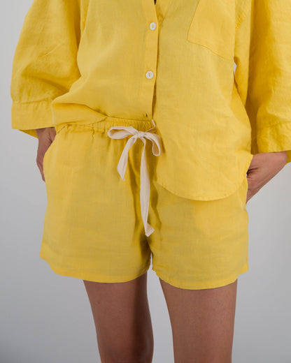 Person wearing a yellow outfit with shorts and a button-up shirt on a gray background