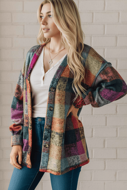 Woman wearing a colorful plaid jacket against a white brick wall.