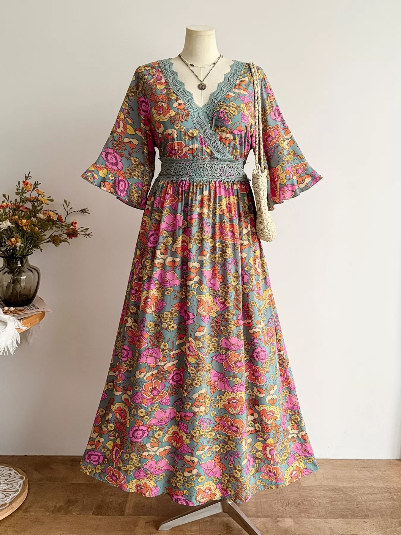 Colorful floral dress on a mannequin against a white wall with a vase of flowers on a table.
