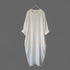 An off-white textured cotton dress with three-quarter sleeves and rolled cuffs, hanging on a metal hanger against a solid dark gray background.