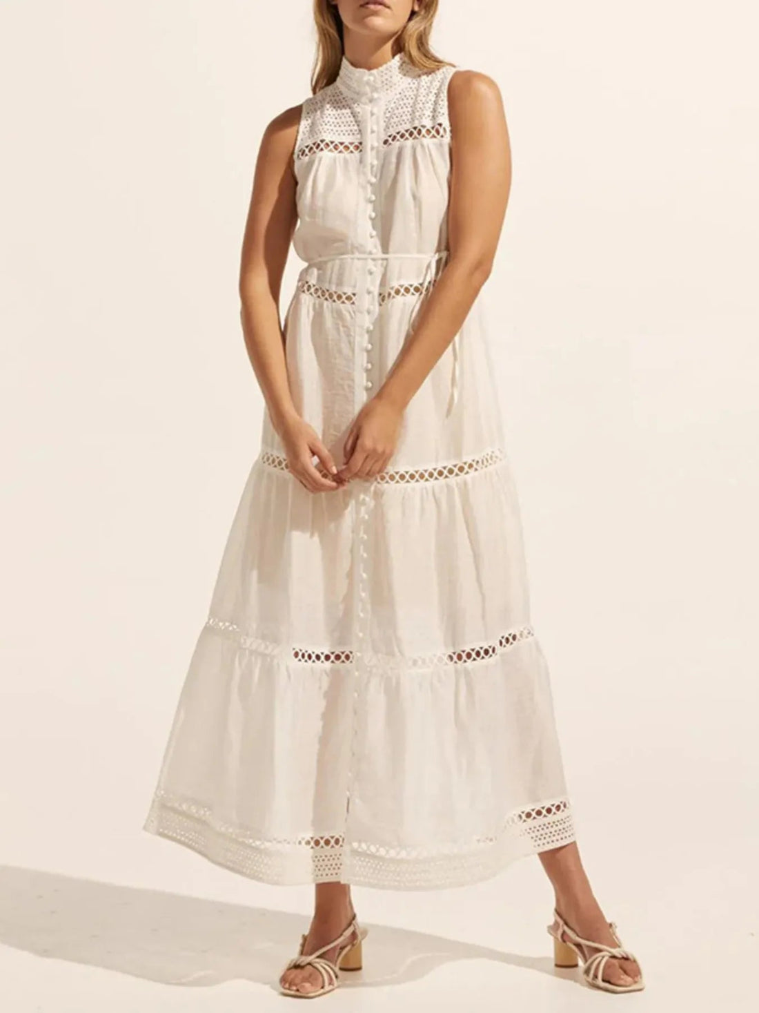 Woman wearing a white sleeveless dress with lace details on a plain background