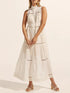 Woman wearing a white sleeveless dress with lace details on a plain background