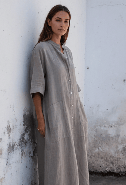 A woman is wearing a long linen dress with a band collar, raglan sleeves, button up.