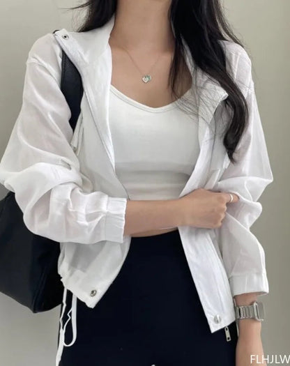 Person wearing a white jacket over a white top with a black bag on a plain background