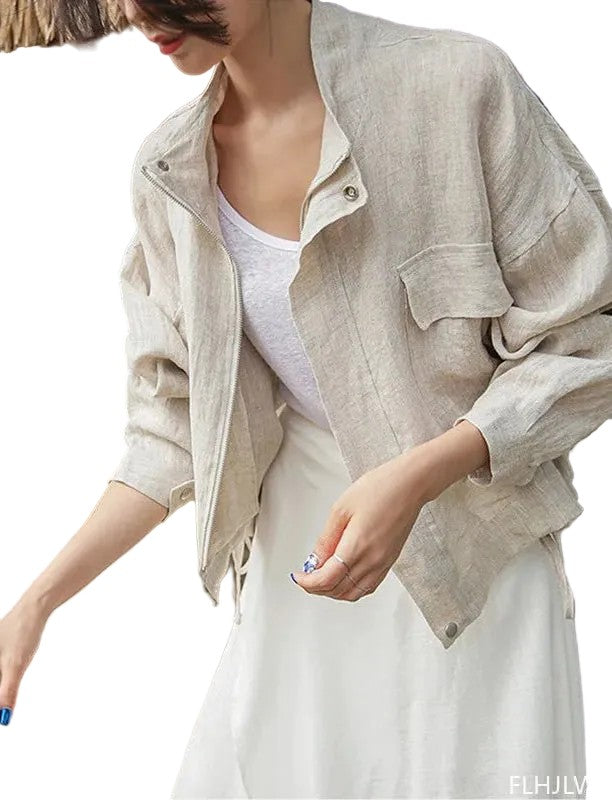 A woman wearing a light beige linen jacket over a white tank top and white skirt, shown from the side against a plain white background.