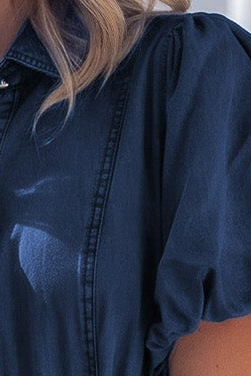 Close-up of a person wearing a dark navy blue short-sleeve top or dress, showing part of the shoulder, sleeve, chest, and blonde hair.