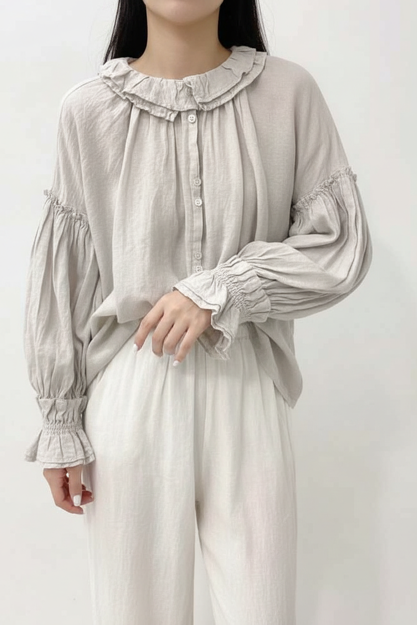 Person wearing a light gray blouse with ruffled collar and cuffs on a white background