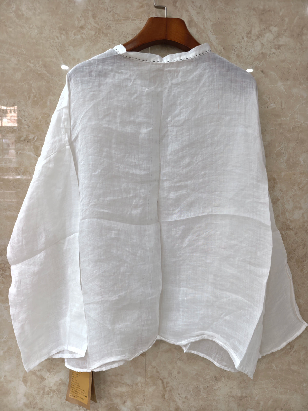 A person wearing a loose white long-sleeve blouse with gathered cuffs and a button placket, paired with a dark skirt, photographed in a dim indoor setting.