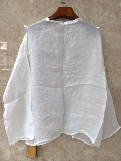 A person wearing a loose white long-sleeve blouse with gathered cuffs and a button placket, paired with a dark skirt, photographed in a dim indoor setting.