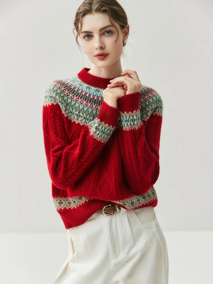 A woman wearing a red cable-knit sweater with a multicolor Fair Isle yoke and hem, paired with white trousers, against a plain light gray studio background.
