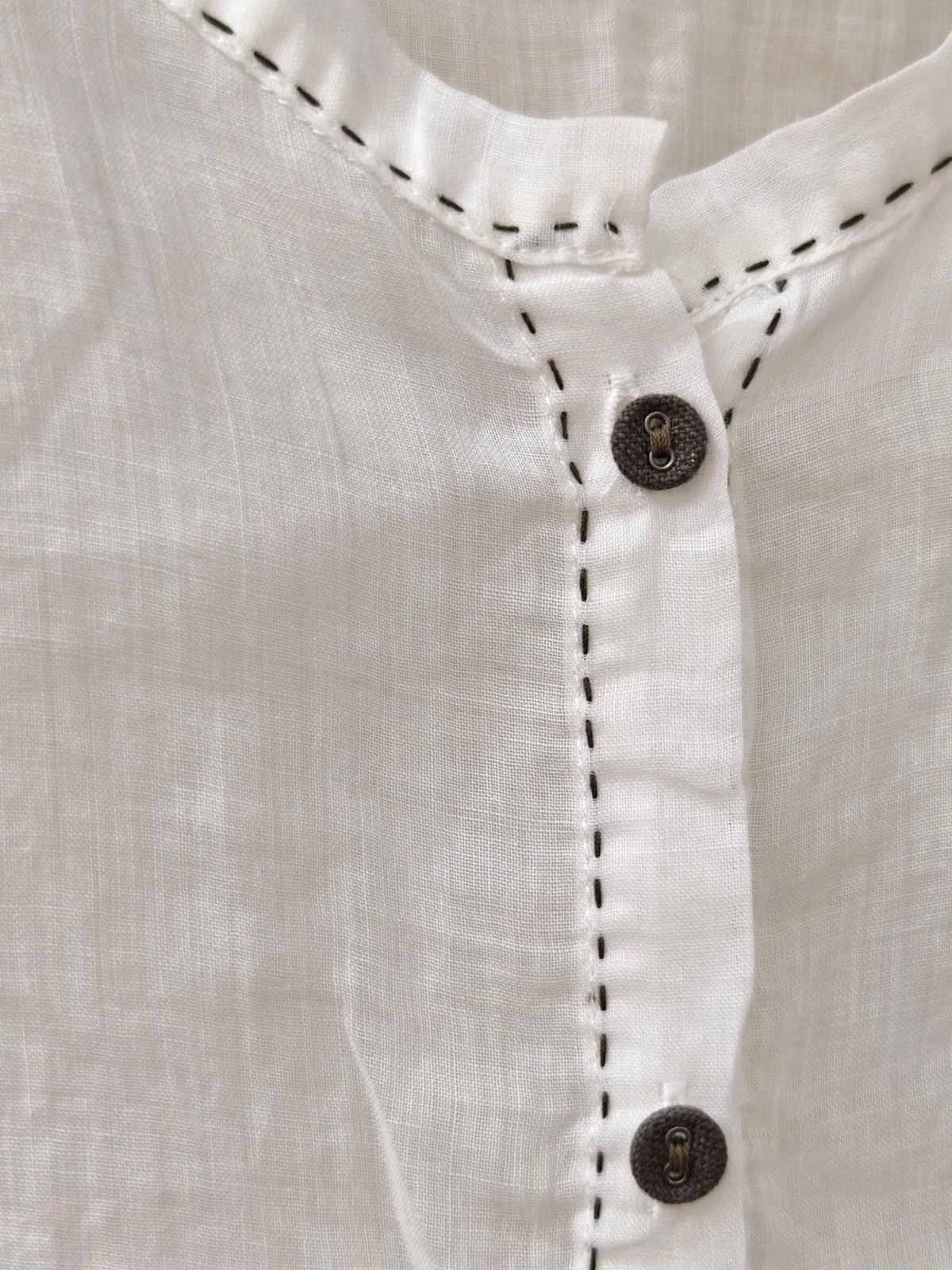 A person wearing a loose white long-sleeve blouse with gathered cuffs and a button placket, paired with a dark skirt, photographed in a dim indoor setting.