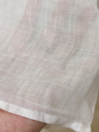 A person wearing a loose white long-sleeve blouse with gathered cuffs and a button placket, 