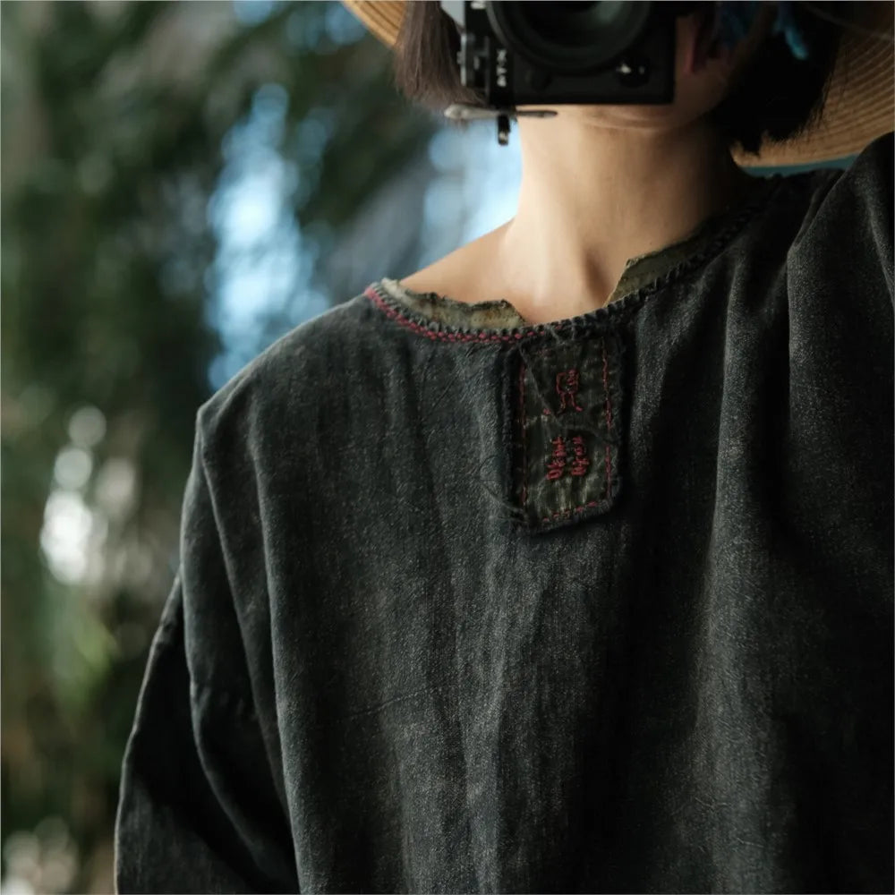 Person wearing a dark green garment with embroidered details, blurred natural background