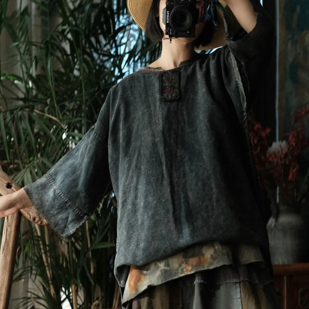 Person wearing a dark gray textured shirt with a floral patterned layer underneath, standing in a natural setting.