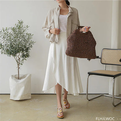 Woman holding a brown woven bag in a minimalistic room with a plant and chair.