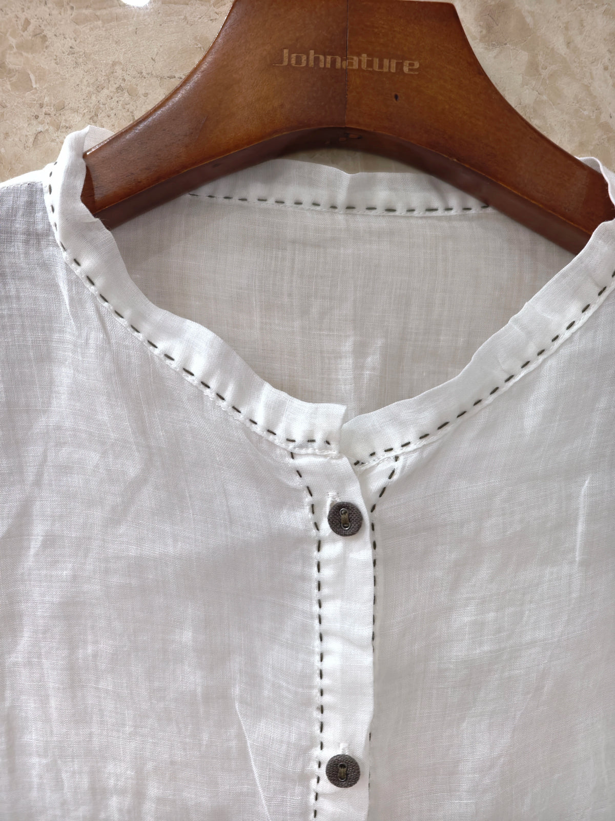 a loose white long-sleeve blouse with gathered cuffs and a button placket, paired with a dark skirt, photographed in a dim indoor setting.